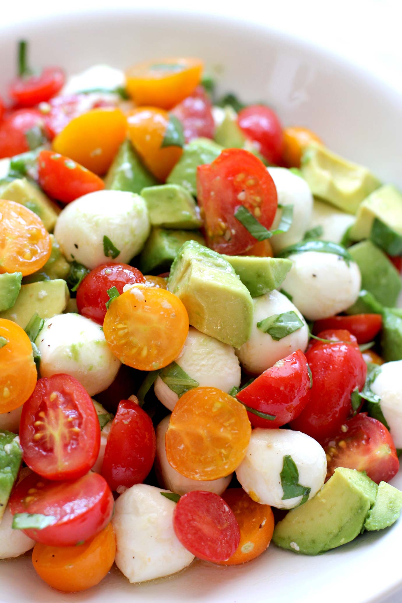 Close up of tomato mozzarella avocado salad in a white bowl.