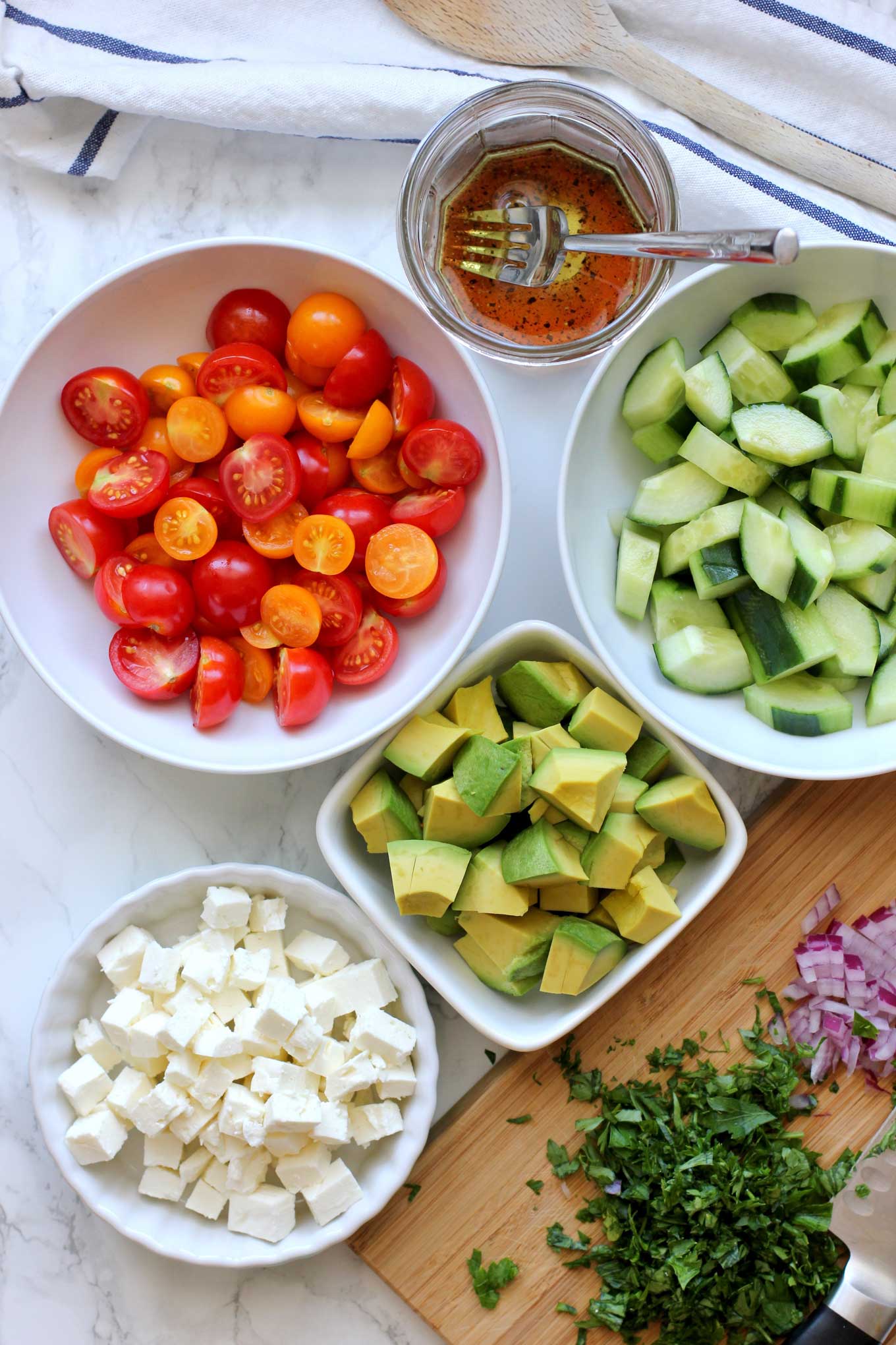 Ingredients to make a tomato, cucumber, avocado salad on a marble countertop.