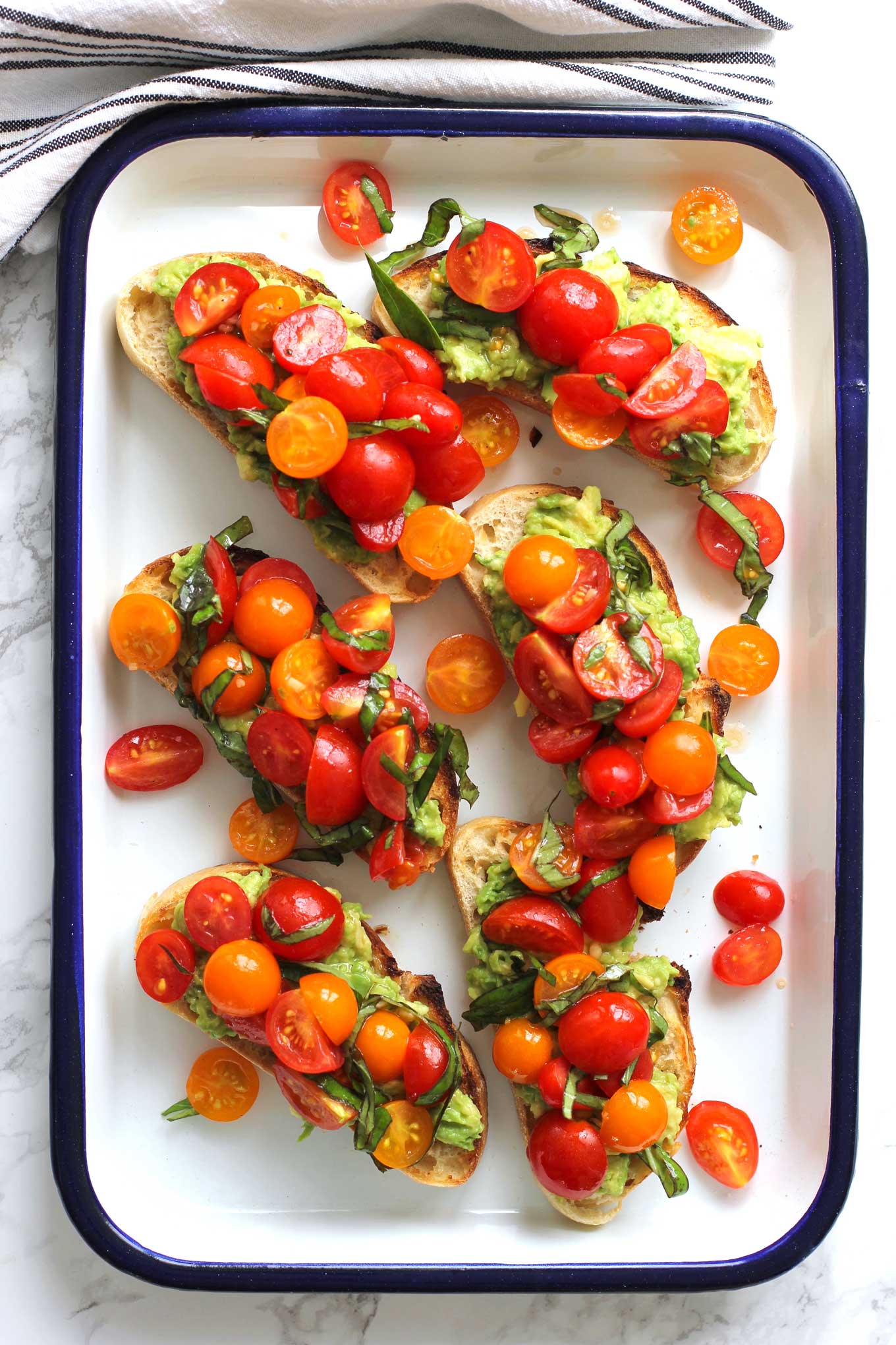 Avocado toast topped with cherry tomatoes on a white pan with a blue edge.