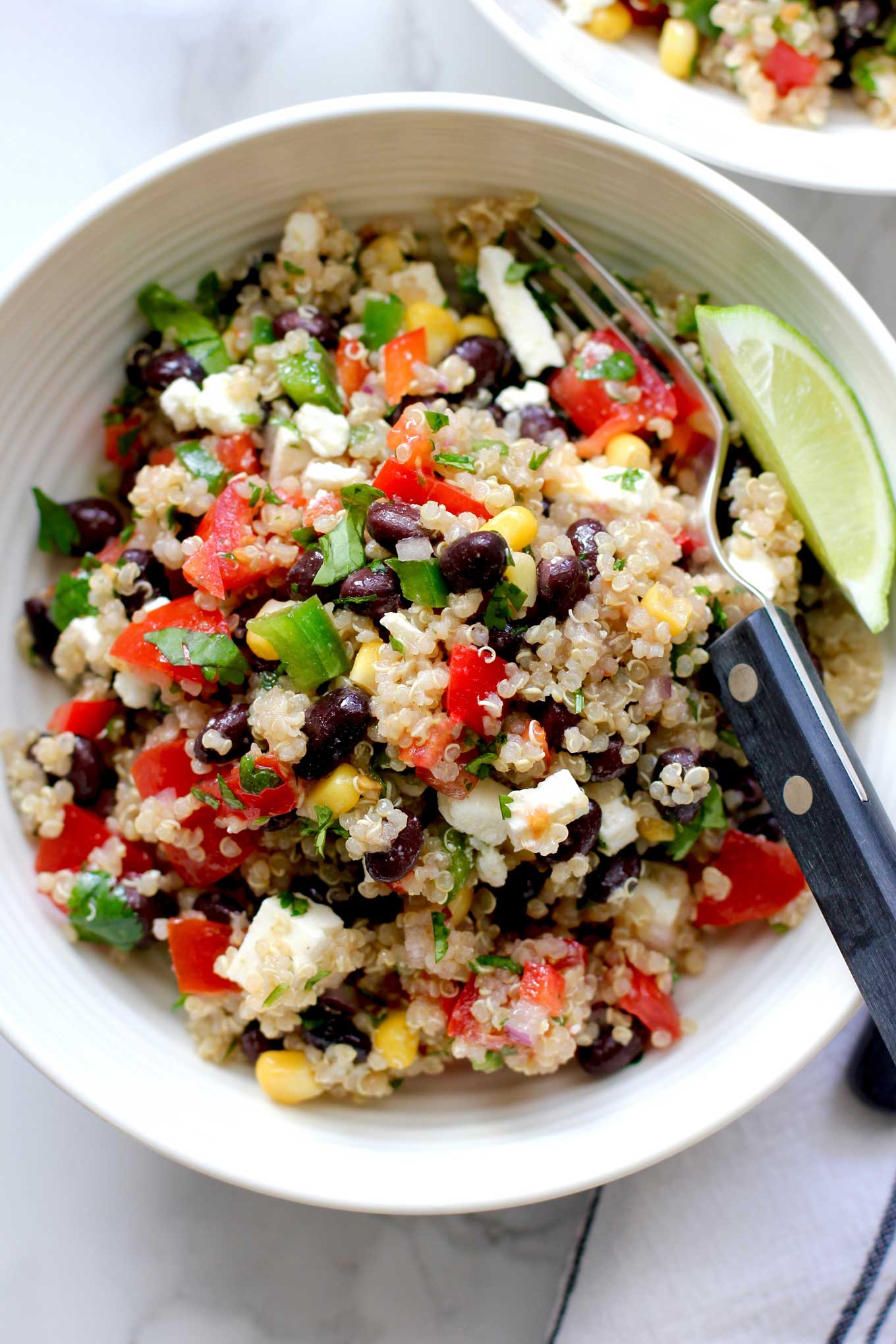 Southwestern quinoa salad in a small white bowl with a fork and slice of lime.