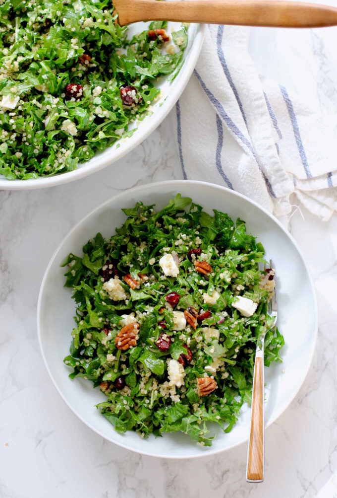 Large and small bowl of quinoa kale salad on a marble countertop.